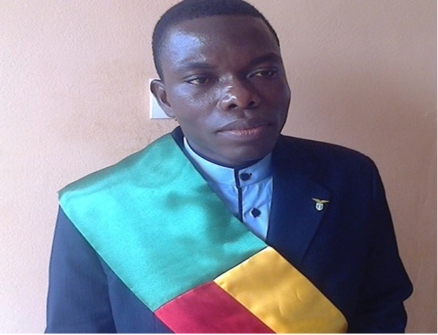 Homme en costume sombre portant une écharpe tricolore verte, jaune et rouge, regardant vers la droite