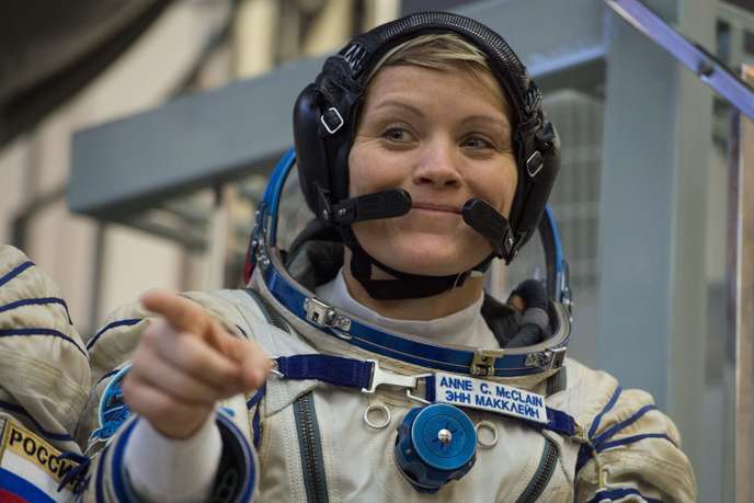 Une personne en combinaison spatiale sourit et pointe du doigt dans un environnement intérieur lié à l’espace