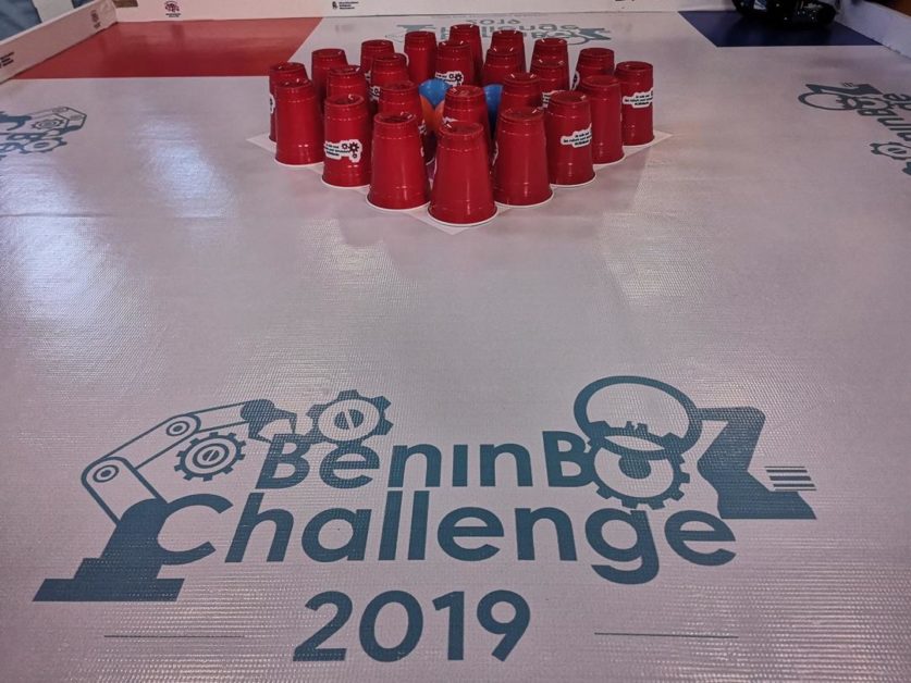 Tasse rouges empilées en forme de pyramide sur une surface marquée BeninBot Challenge 2019 avec motifs robotiques