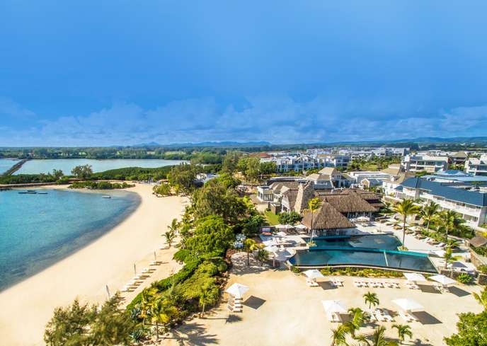 Plage de sable blanc bordée de cocotiers et d’un complexe hôtelier avec piscines et chaises longues sous un ciel bleu