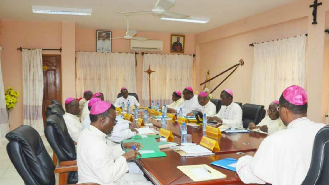 Un groupe de religieux en soutanes blanches et coiffés de zucchettos violets assis autour d'une grande table lors d'une réunion.