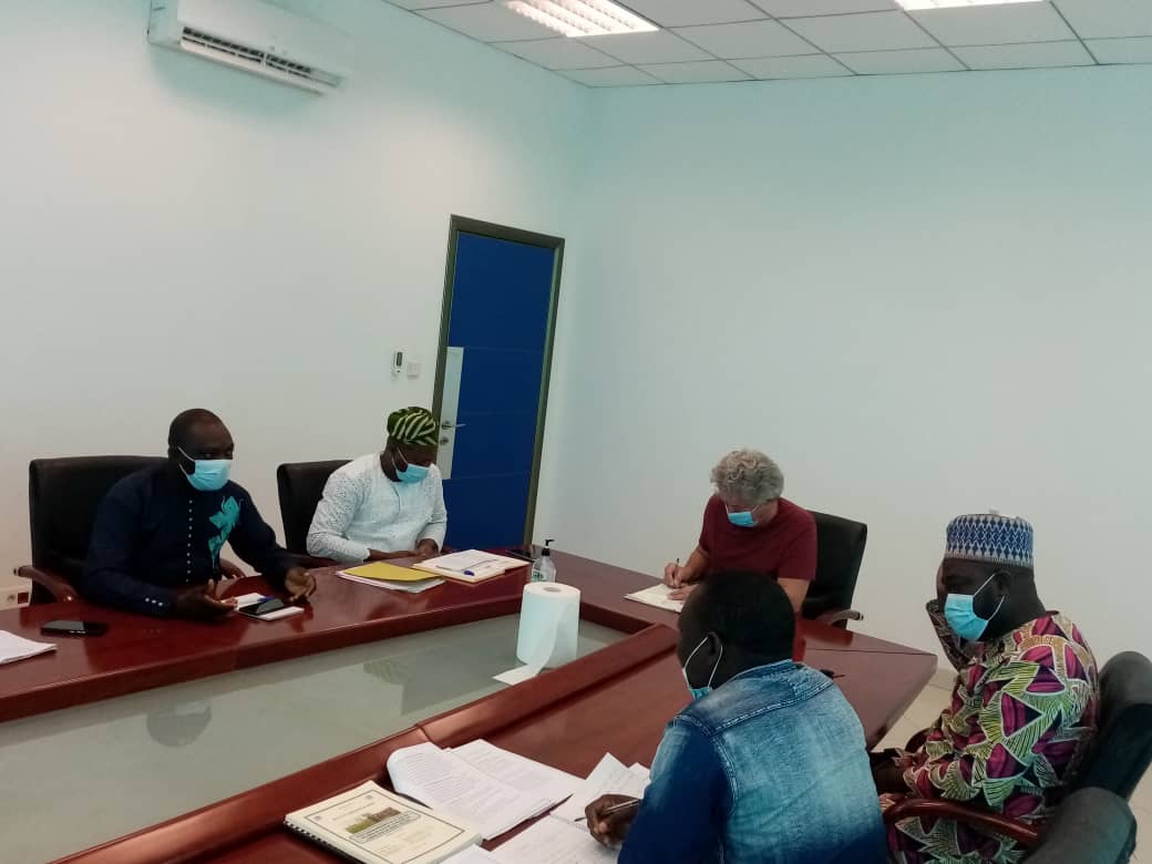 Quatre hommes assis autour d'une table en réunion dans une salle avec murs blancs et visièrés faciaux en place