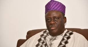 Homme en tenue traditionnelle africaine et chapeau violet, assis sur un fauteuil marron claire