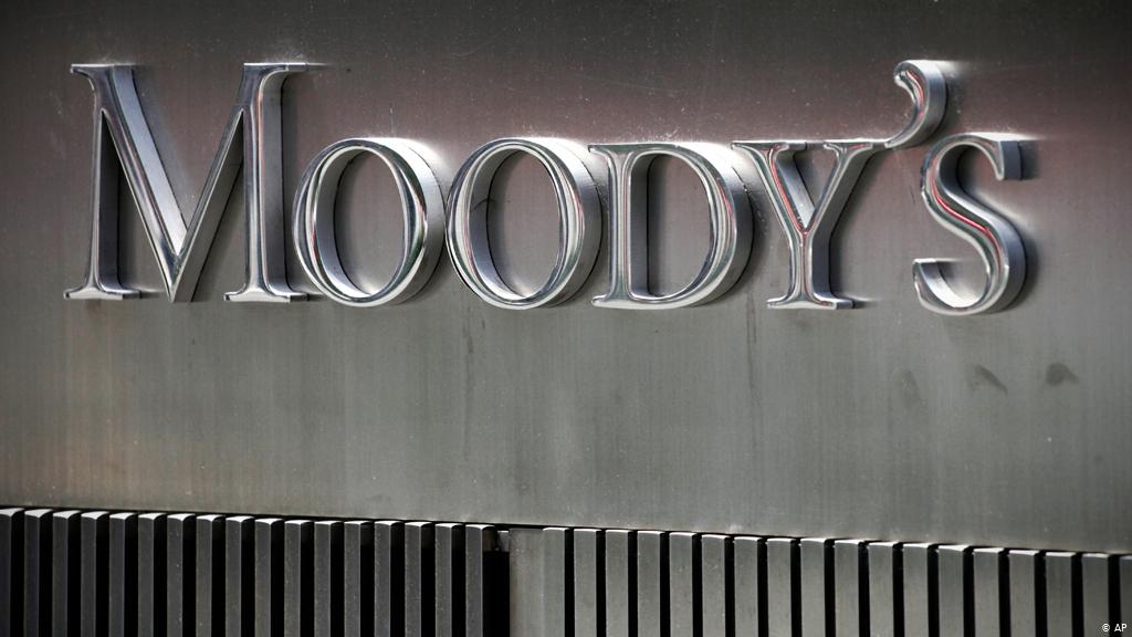 Logo métallique de Moody’s fixé sur une façade grise avec des lames noires en dessous