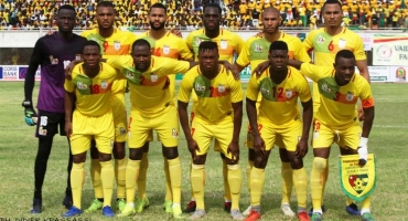 Onze joueurs de football posant en tenue jaune sur un terrain avant un match devant des tribunes remplies de spectateurs