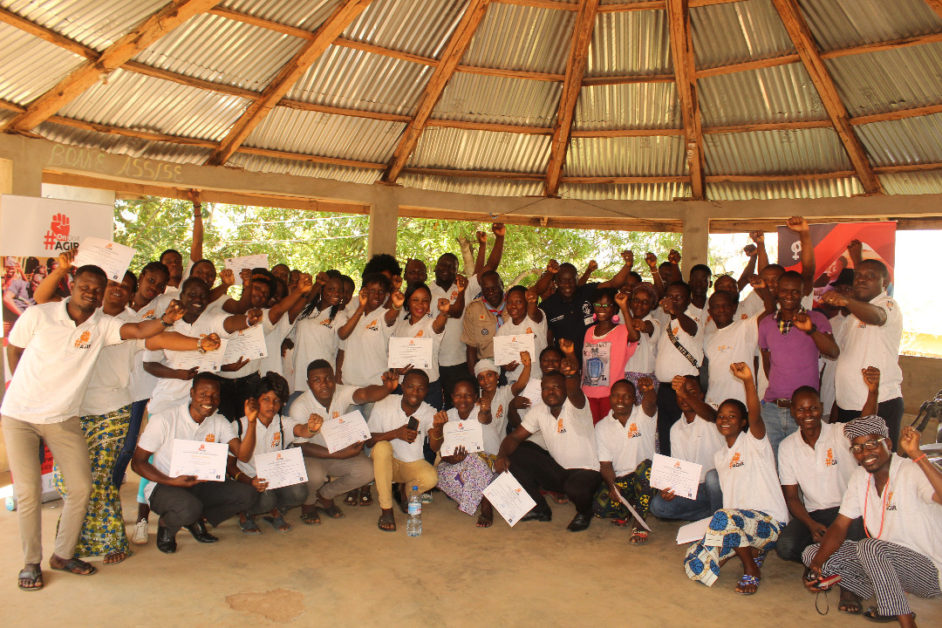 Groupe de jeunes souriants en tenues blanches posant avec des certificats sous une structure en bois circulaire