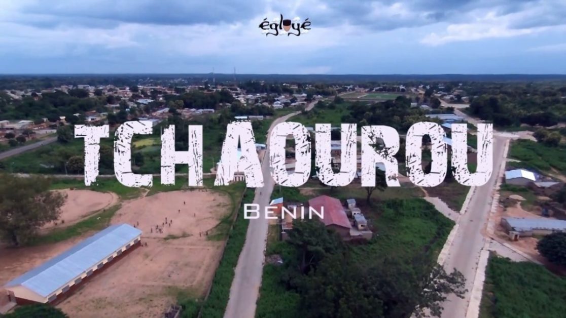 Vue aérienne d’une ville avec routes, bâtiments et espaces verts sous un ciel nuageux, inscriptions TCHAUROU Bénin au centre