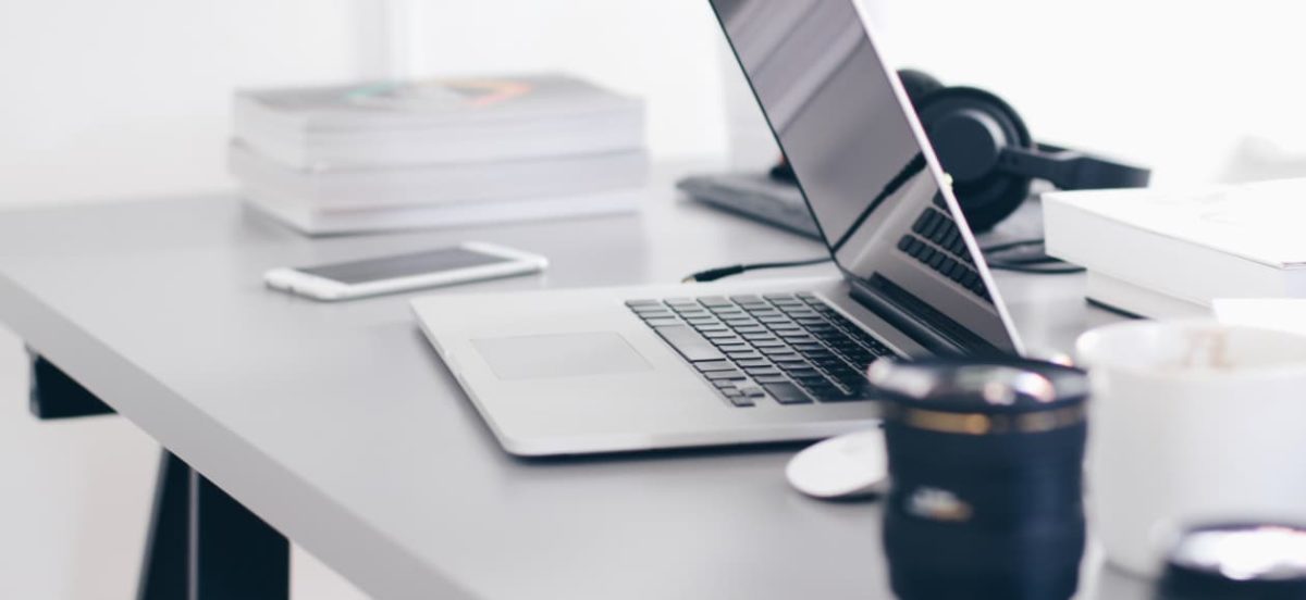 Bureau avec ordinateur portable ouvert, smartphone, tasse et piles de documents sur une table claire