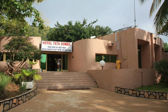 Façade d'un bâtiment avec enseigne Hôtel Tata Somba entouré de végétation et d'un escalier menant à l'entrée