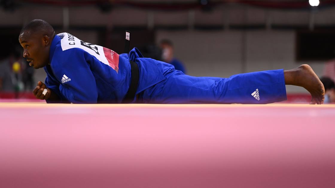 Judoka allongé face contre le sol en kimono bleu sur le tatami lors d’un combat