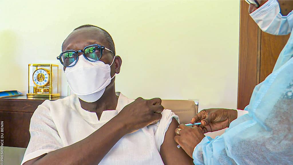 Un homme en lunettes et masque reçoit une injection dans le bras par un professionnel en tenue médicale bleue