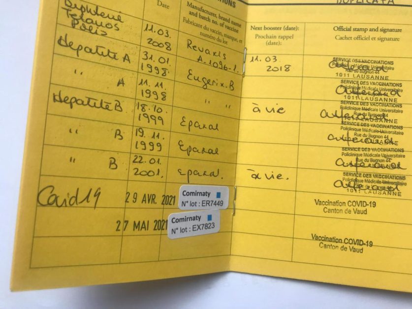 Carnet de vaccination jaunâtre avec plusieurs tampons et deux autocollants de vaccination COVID-19 visibles