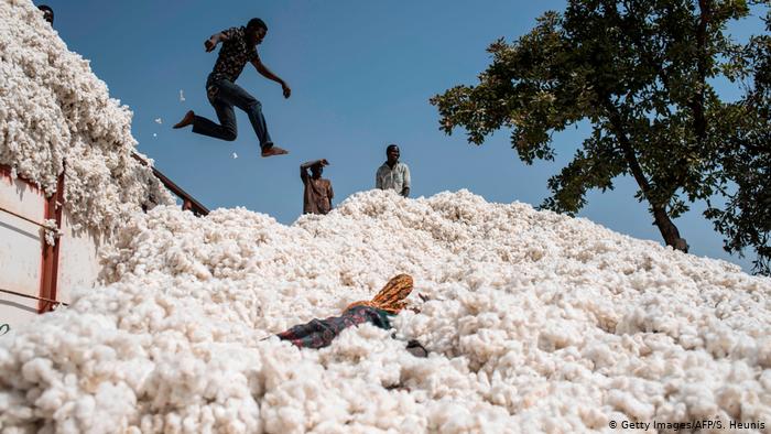Un homme saute dans une immense pile de coton blanc sous un ciel bleu avec deux autres personnes debout à proximité