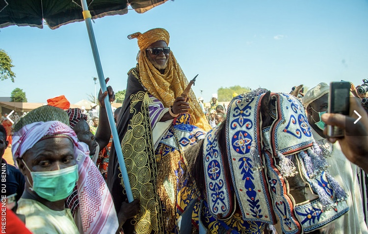 Un homme vêtu de vêtements traditionnels dorés sur un cheval décoré lors d’une fête en plein air avec foule autour