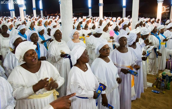 Un grand groupe de femmes en robes blanches et coiffées de turbans participent à une cérémonie religieuse en intérieur