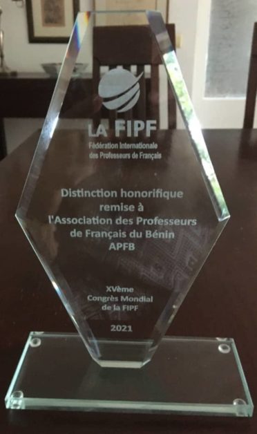 Trophée en verre gravé à la main posé sur une table avec le logo de la FIFPE et un texte d'hommage à une association de professeurs