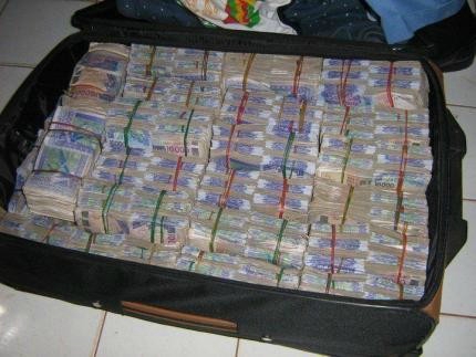 Valise ouverte contenant de nombreuses liasse de billets de banque empilés et attachés par des élastiques colorés