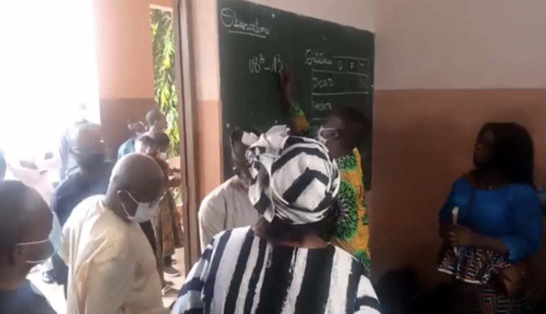 Des candidats portant des masques sont rassemblés près d un tableau noir dans une salle d examen.