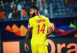 Un joueur en maillot jaune numéroté 14 regarde sur le côté sur un terrain de football.