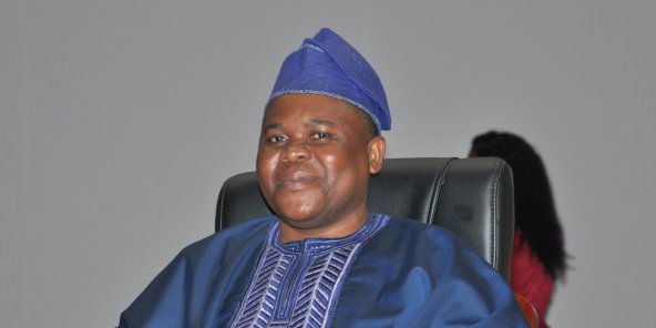 Homme souriant habillé en tenue traditionnelle bleue et coiffé d'un bonnet assorti assis sur une chaise noire
