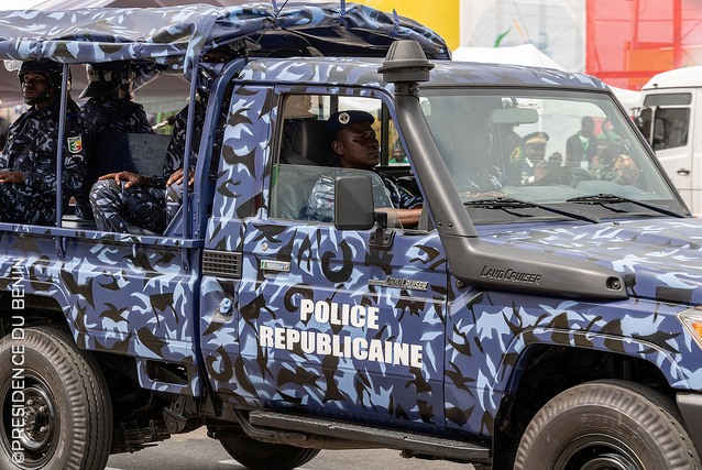 Véhicule militaire bleu camouflage marqué Police Républicaine avec plusieurs policiers à bord en action en milieu urbain