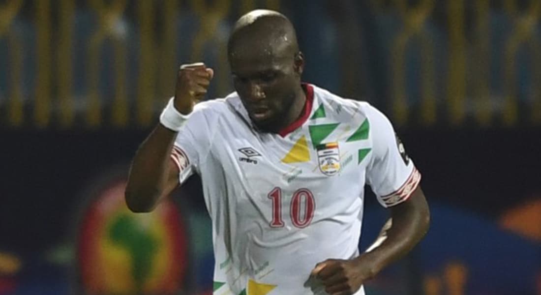 Un footballeur en maillot blanc blanc lève le poing en signe de victoire sur le terrain de nuit