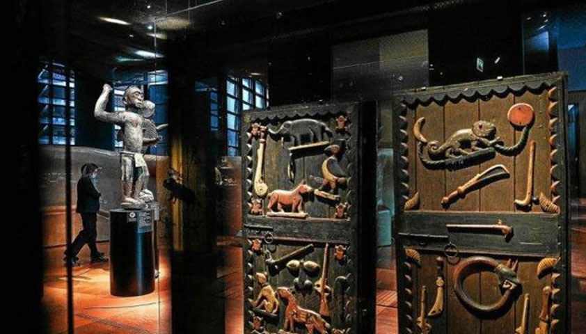 Salle d’exposition obscure avec sculptures et panneaux sculptés éclairés au mur et sur socle