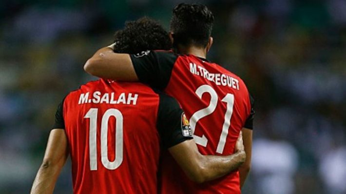 Deux joueurs de football en maillot rouge avec noms et numéros vus de dos s'enlacent sur le terrain