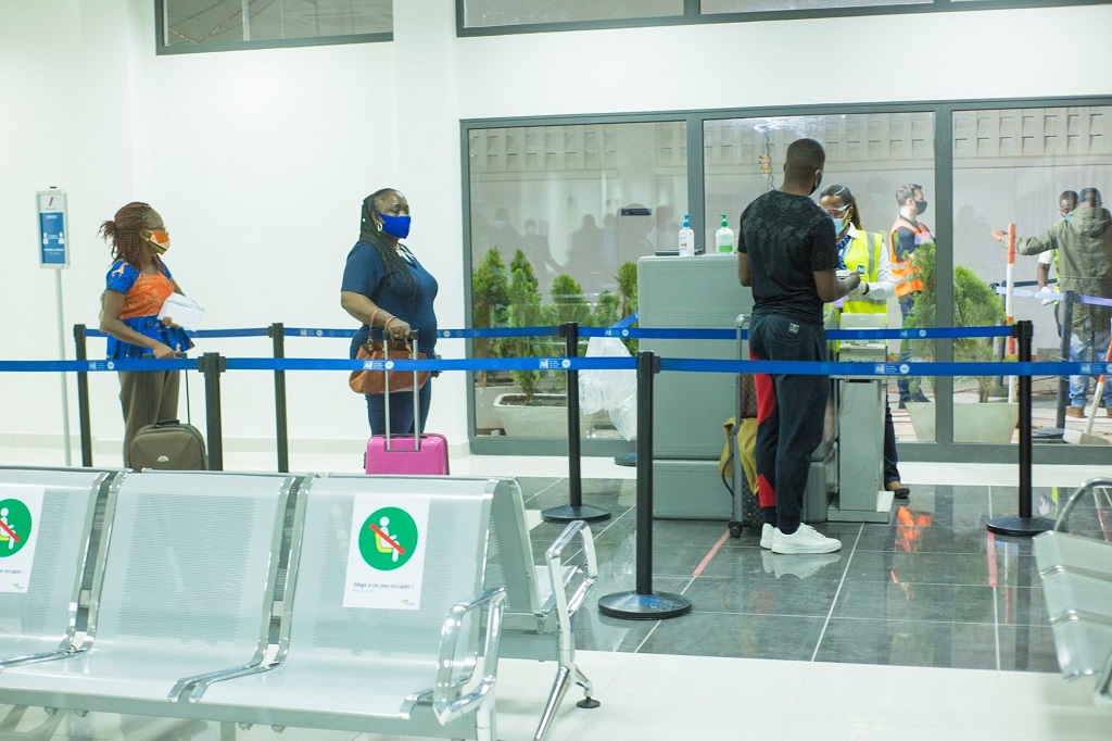 Des passagers en file d attente au contrôle de sécurité dans un hall d aéroport avec des agents en tenue et masques sanitaires