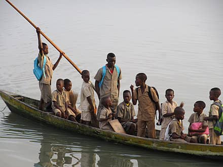 Onze écoliers en uniforme beige naviguent en pirogue sur une étendue d'eau calme un garçon manœuvre la rame debout à l'arrière
