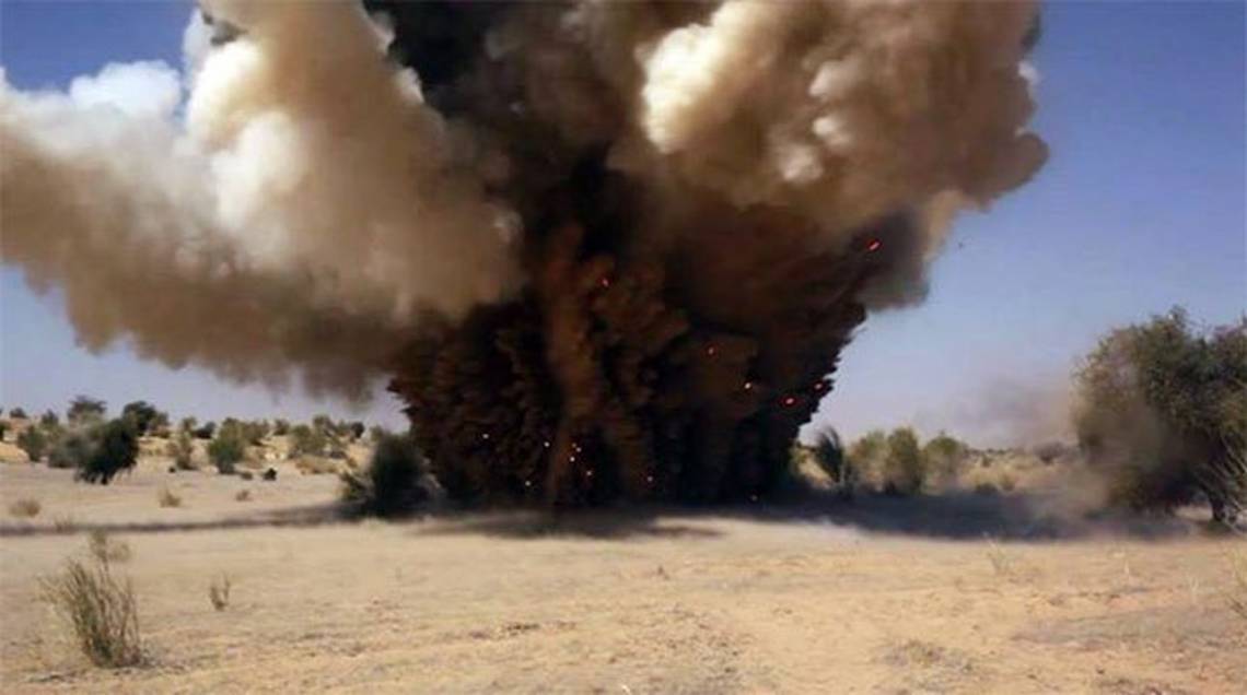 Explosion en cours avec un nuage de fumée épais et des flammes dans un paysage sec avec des arbres épars