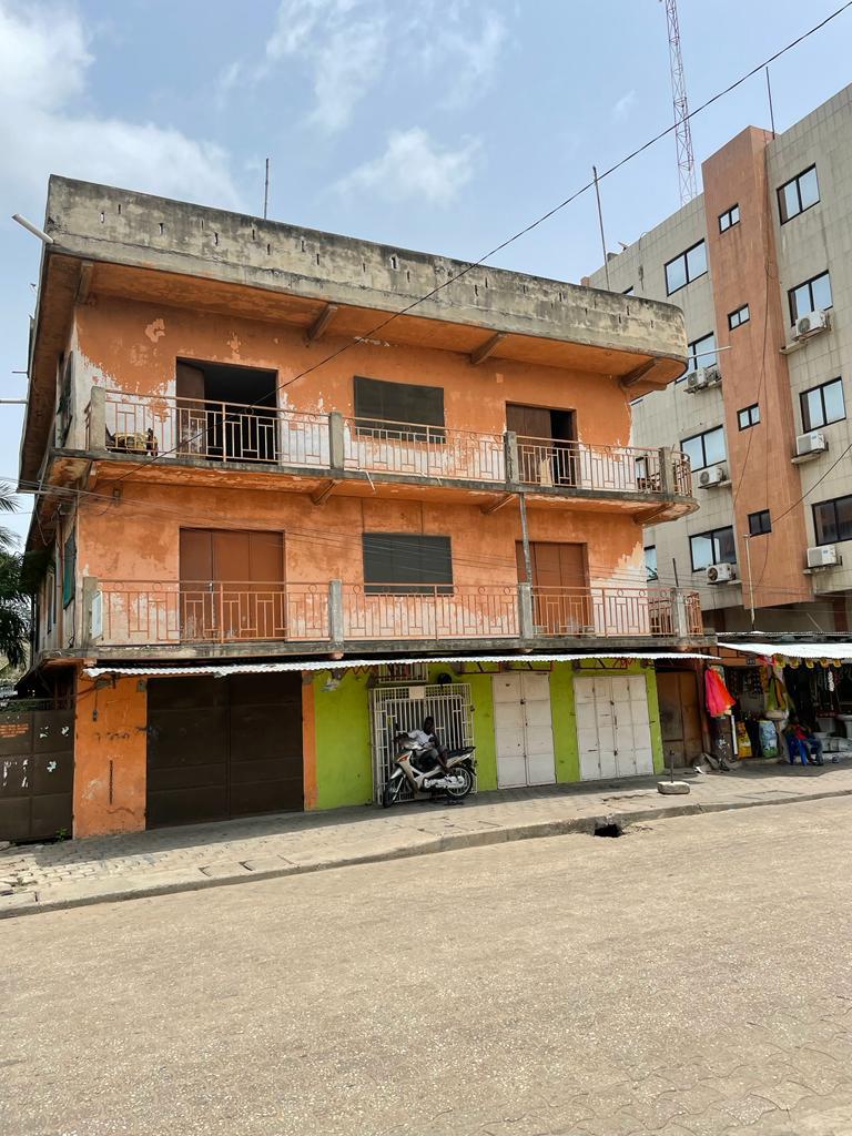 Immeuble ancien orange à deux étages avec balcons métalliques et commerces fermés au rez-de-chaussée sur une rue pavée