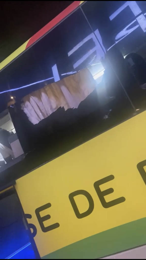 Fenêtre latérale d’un bus de couleur jaune endommagée avec un grand trou dans la vitre en plein soir