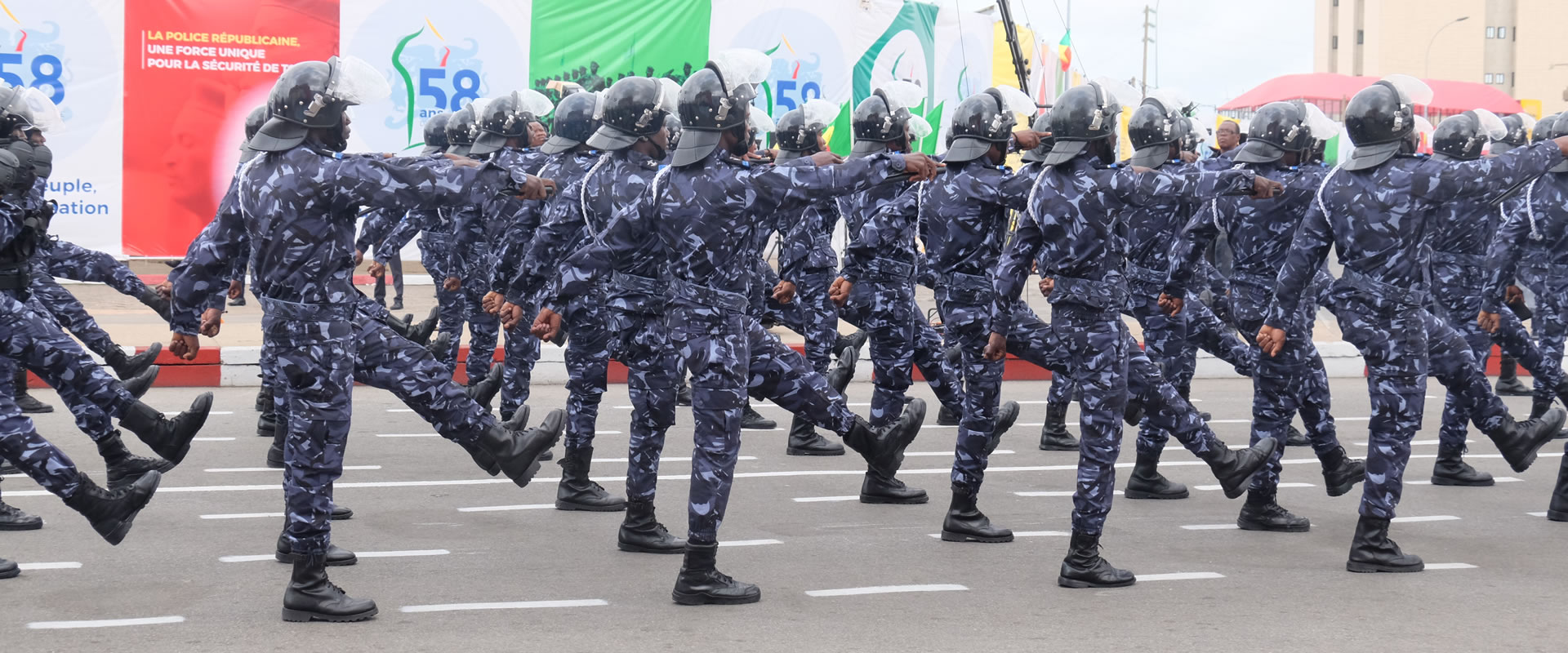 Un groupe de personnes en uniforme bleu camouflage avance en formation lors d’un défilé sur une route urbaine