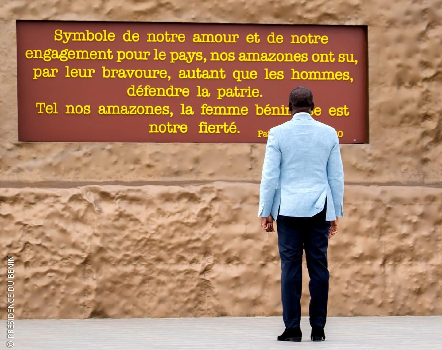 Un homme en veste claire regarde un panneau rouge avec un texte jaune contre un mur beige texturé