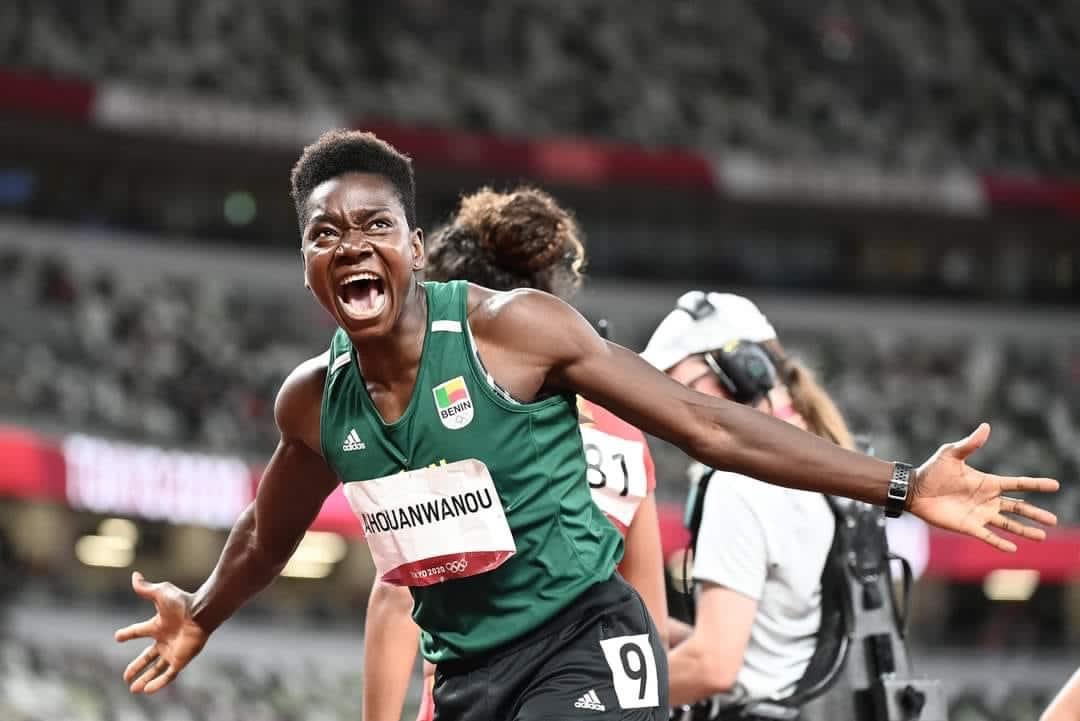 Athlète en tenue verte au numéro 9 célèbre sa performance avec énergie sur une piste d’athlétisme en stade presque vide