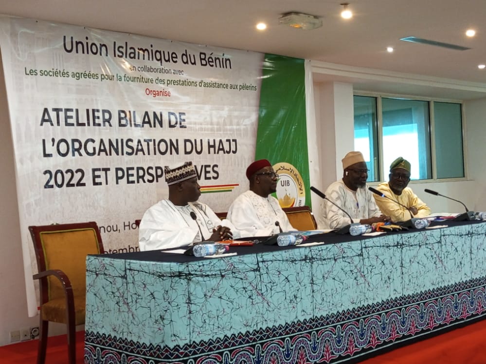 Quatre hommes en tenue traditionnelle assis derrière une table lors d un atelier avec une bannière sur l organisation du Hajj 2022