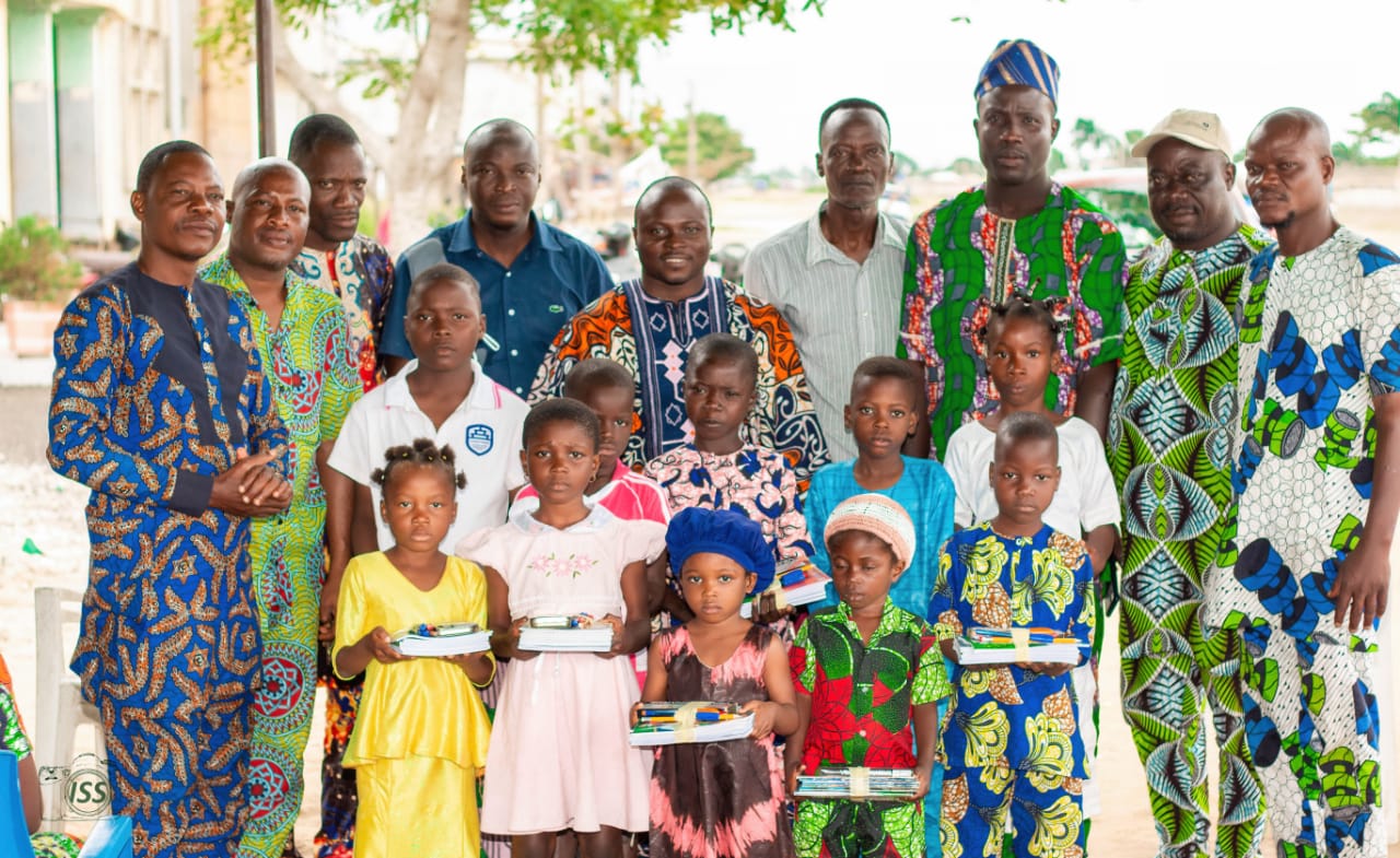 Un groupe d’adultes et d’enfants pose dehors, les enfants tenant des kits scolaires dans leurs mains