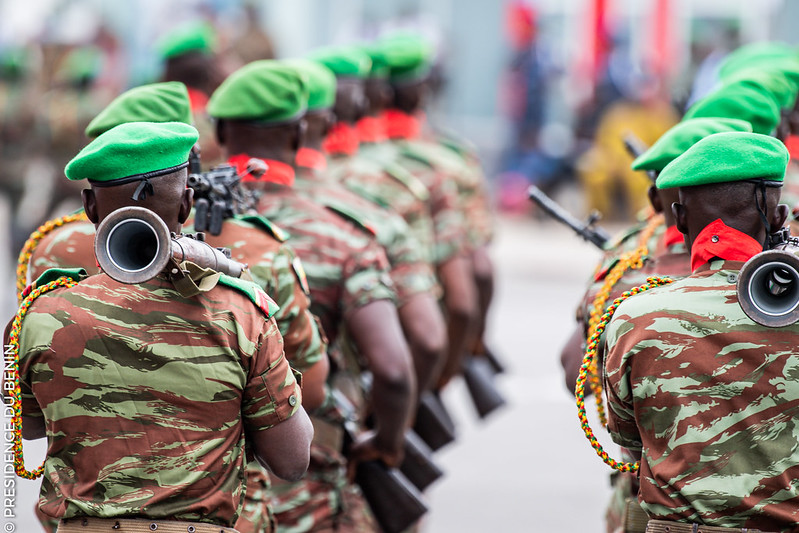 Soldats en uniforme militaire et bérets verts alignés en formation marchant de dos sur une voie urbaine