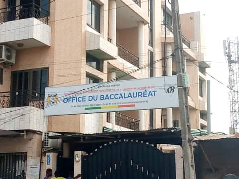 Entrée d'un bâtiment avec une bannière affichant le texte « OFFICE DU BACCALAURÉAT » suspendue au-dessus d'une porte noire.</s>