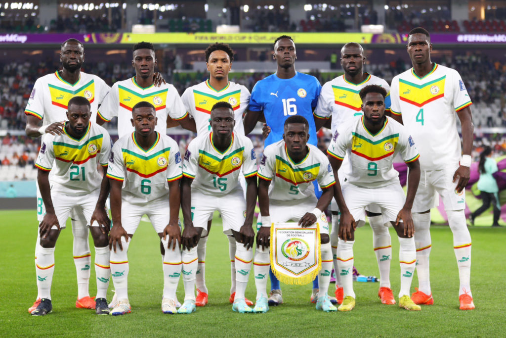 Onze joueurs de football en tenue blanche avec bandes vertes et jaunes posant sur le terrain avant un match officiel