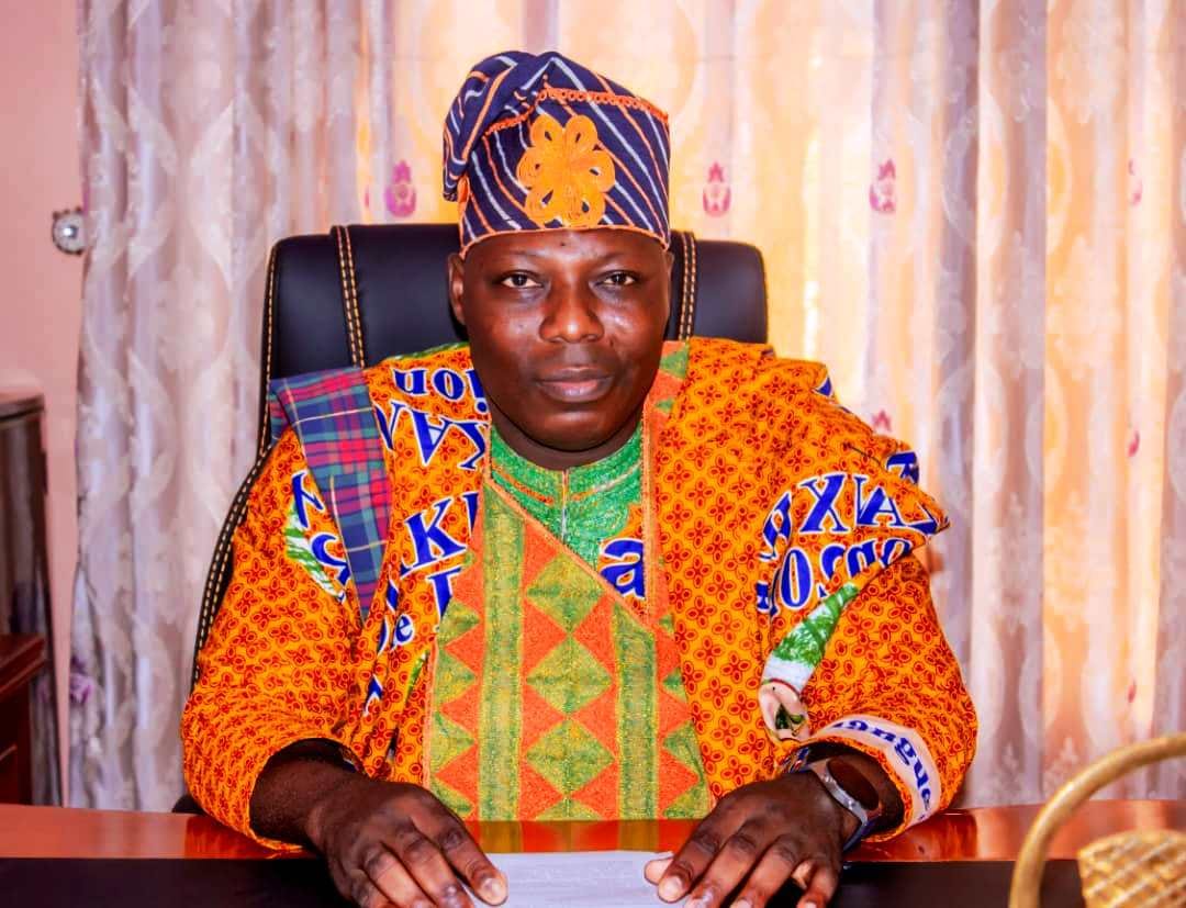 Homme habillé en tenue colorée traditionnelle africain assis derrière un bureau avec des rideaux clairs en arrière-plan
