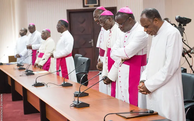 Hommes en vêtements religieux debout en silence dans une salle de réunion devant une table équipée de microphones