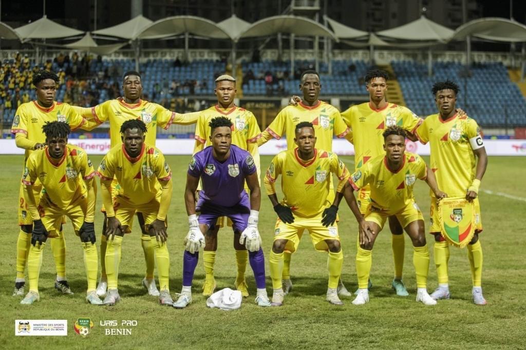 Onze joueurs de football posent sur un terrain avec des maillots jaunes et un jeu de lumière nocturne dans un stade quasiment vide