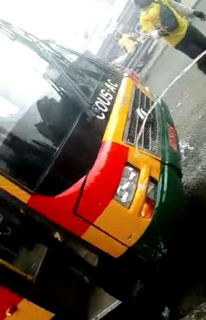 Bus vert, jaune et rouge fumant à l'avant droit avec deux personnes en arrière-plan en tenue jaune