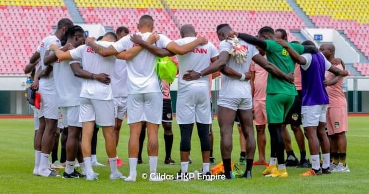 Groupe de joueurs de football en cercle bras dessus bras dessous sur un terrain de stade vide.