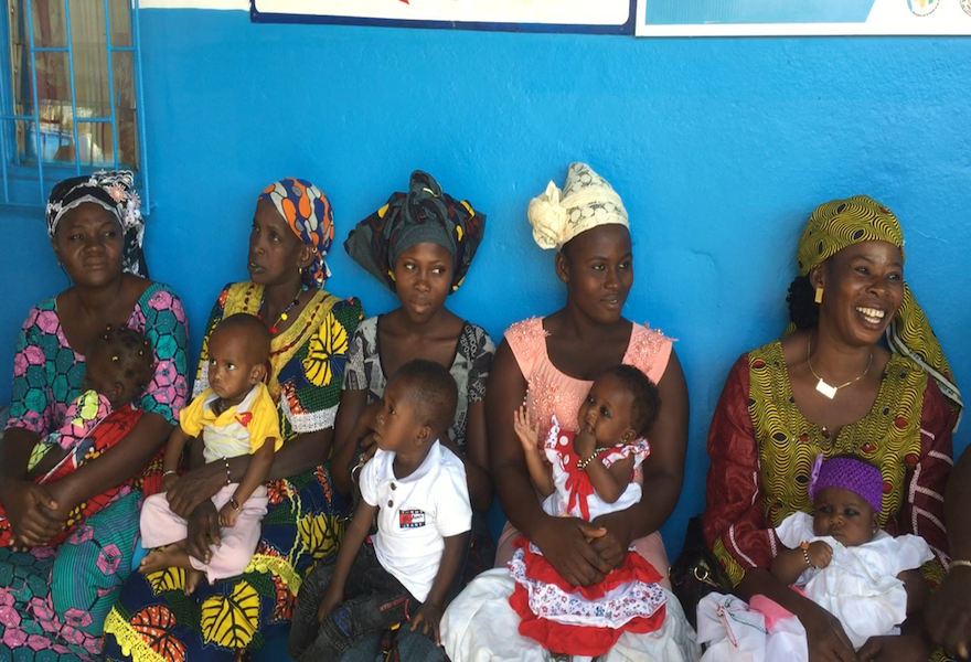 Femmes assises côte à côte portant des vêtements colorés tenant des enfants sur leurs genoux dans une pièce aux murs bleus