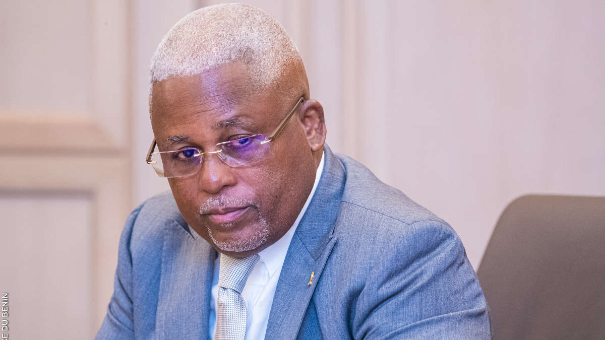 Homme d’affaires sérieux en costume bleu et lunettes assis face à un mur clair dans une salle de réunion