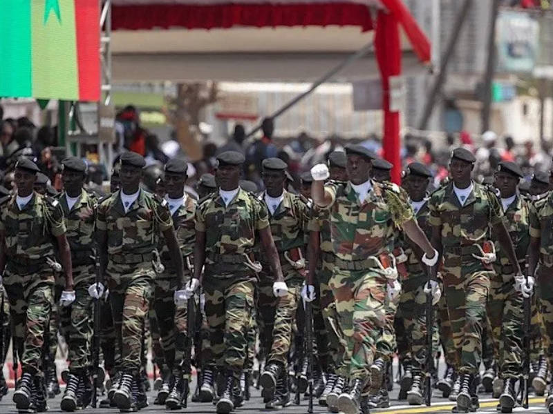 soldats en uniforme de camouflage défilant en formation serrée en milieu urbain avec drapeau en arrière-plan