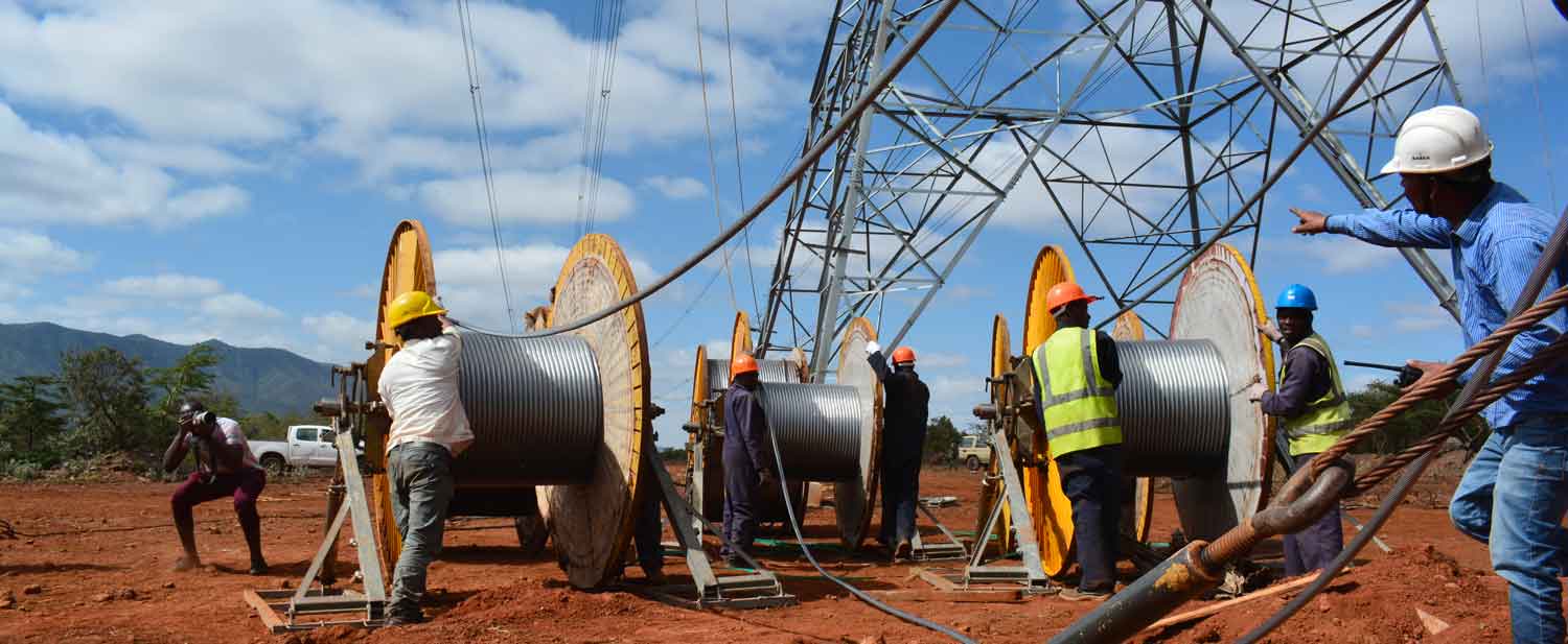 Plusieurs ouvriers en tenue de chantier déroulent de gros câbles électriques près d’une grande structure métallique de pylône haute tension